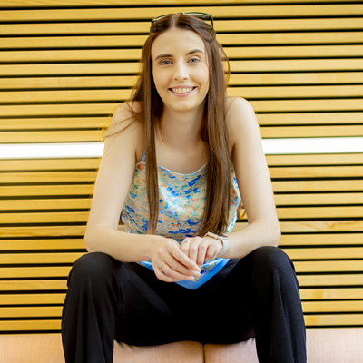 A female student with long brown hair is smiling while sitting on the back of a sofa