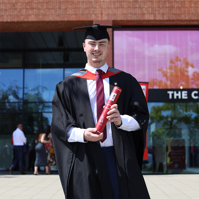 Corey Meir in his graduation gown and cap holding a scroll