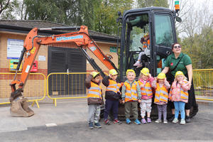 A group of children in hard hats standing in front of a digger