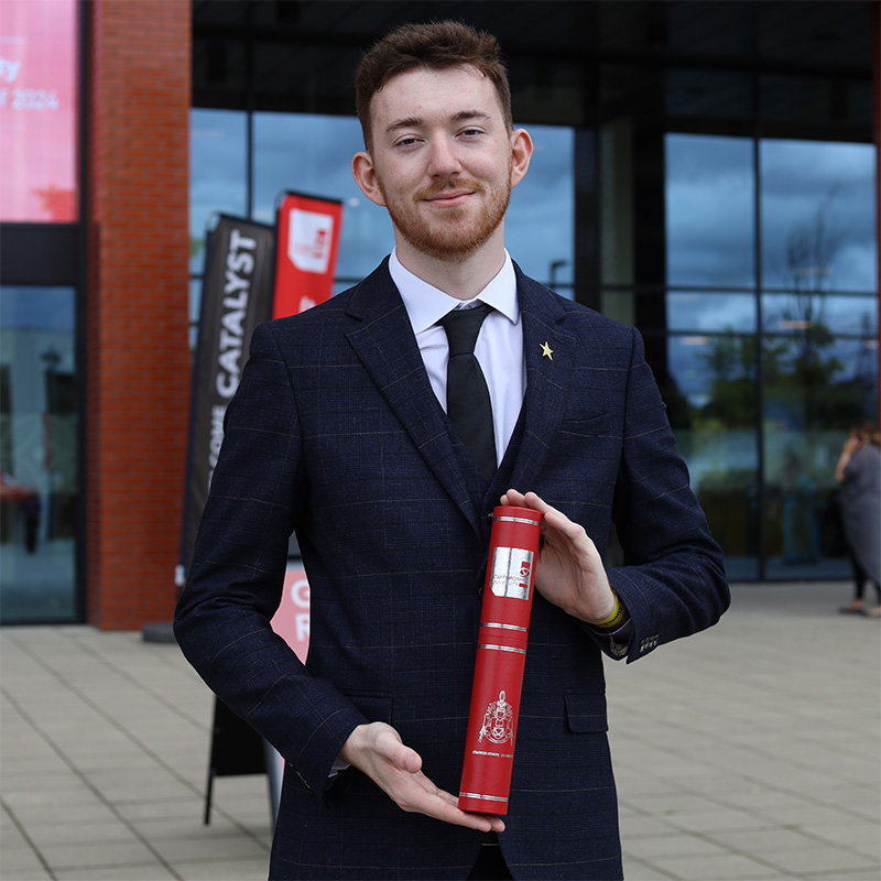 Joshua Griffin-Meek pictured wearing a suit and holding a graduation scroll