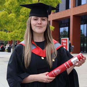 Kerry Moynihan in a gratduaion cap and gown holding a scroll