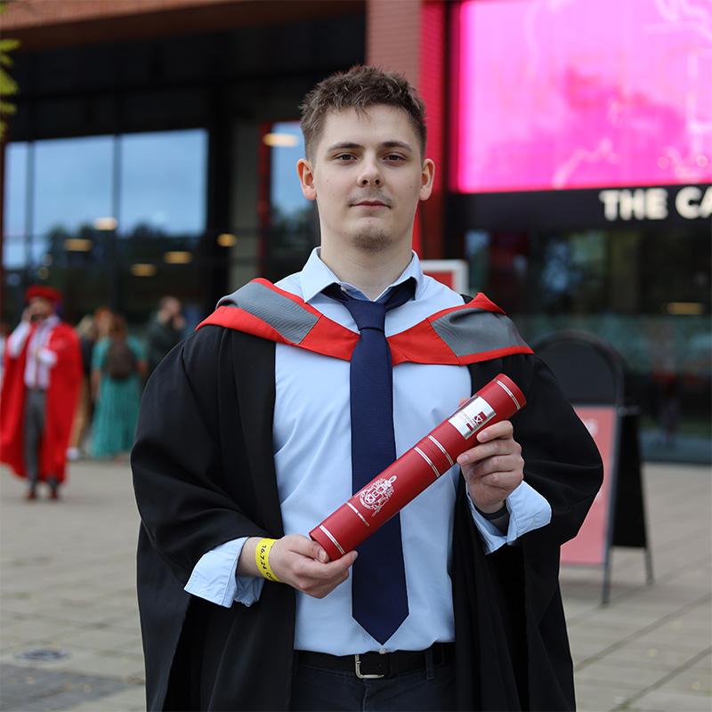 Louis Stonehouse-Gusewski in his graduation gown holding a scroll