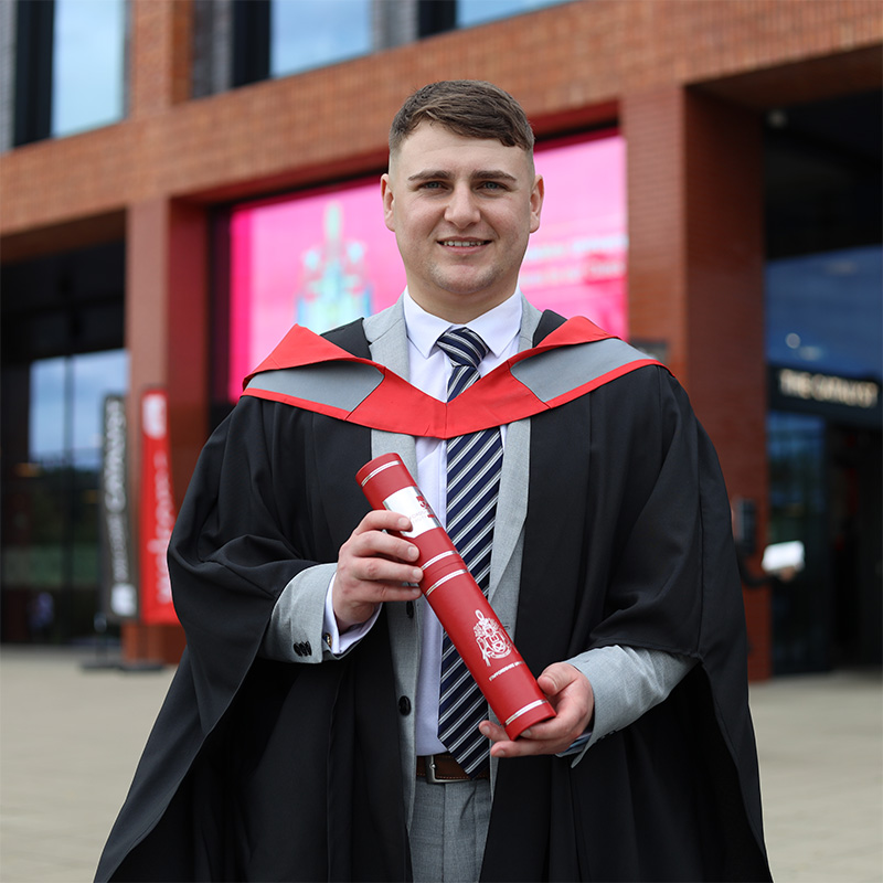 Ryan Zwetschnikow in his graduation robes holding a scroll