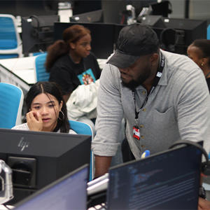 A male teacher assisting a female student in coding.