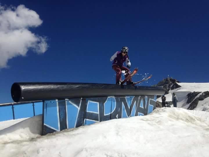 Freestyle skier slides along a black rail on a snowy slope beneath a deep blue sky.