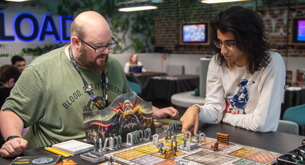 Two men are focussing whilst playing a table top strategy game in the Reload cafe area