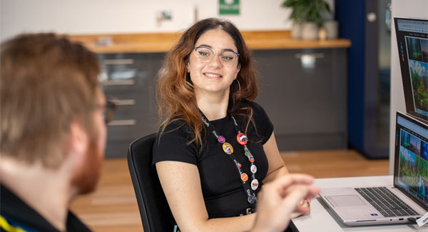 A female is smiling and in conversation with a man in a modern office area