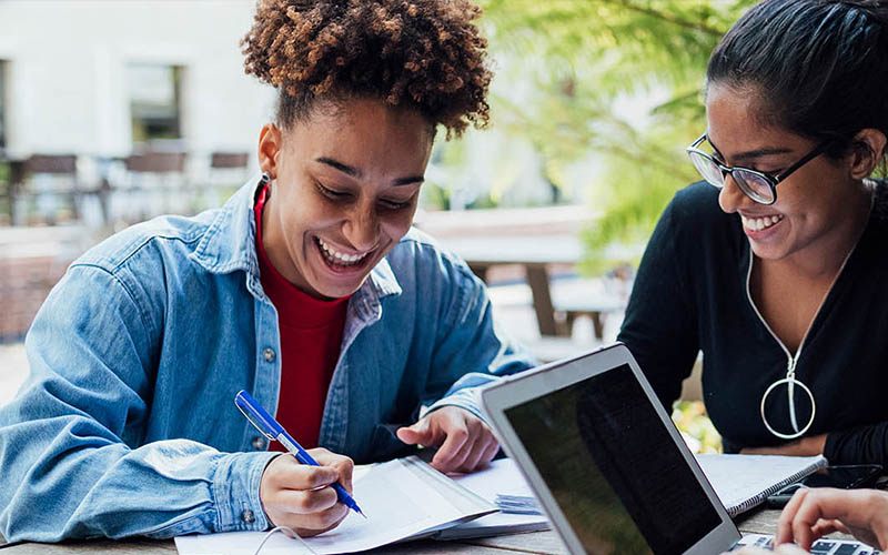 female students working outdoors with laptops and notebooks