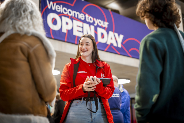 A female student ambassador wearing red uniform is chatting to open day visitors