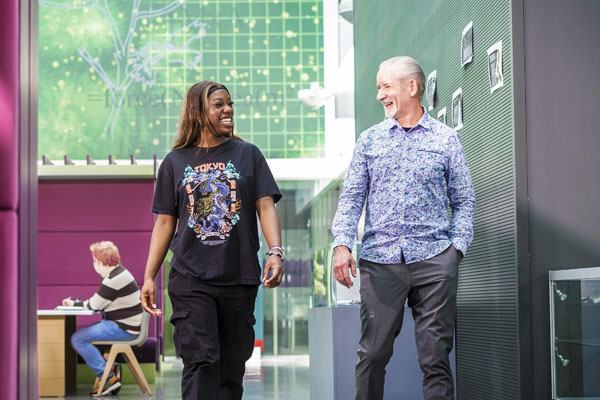 A young female and mature male student are chatting whilst walking in a modern open space