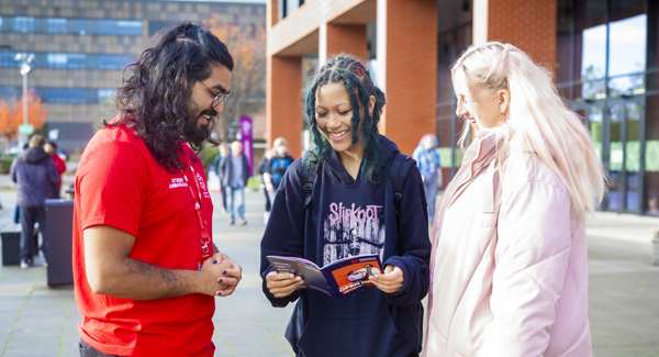 A student ambassador wearing a red uniform is providing open day guidance to two female visitors on campus ground