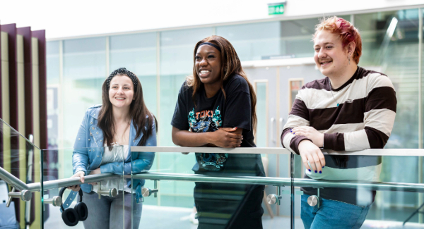 three students stood leaning on a rail